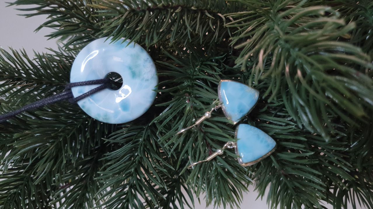 Ein blauer Lapis-Lazuli-Halsanhänger und Ohrringe liegen auf einem grünen Weihnachtsbaum. Der Anhänger hat ein Loch und die Ohrringe sind tropfenförmig.