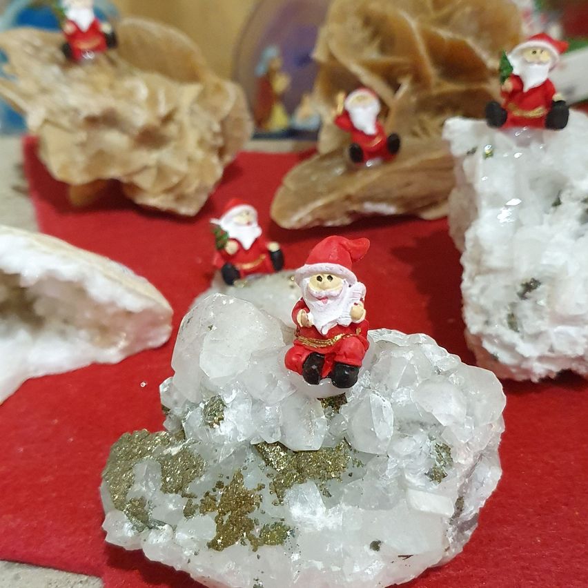 Verschiedene Kristallformationen und Miniatur-Weihnachtsmannfiguren ruhen auf einem roten Tuch. Jede Weihnachtsmannfigur befindet sich auf einer anderen Kristallstruktur.