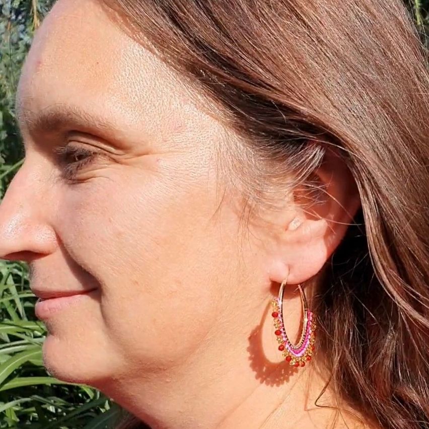Nahaufnahme des Gesichts einer Frau mit braunem Haar, die bunte Perlenohrringe trägt.