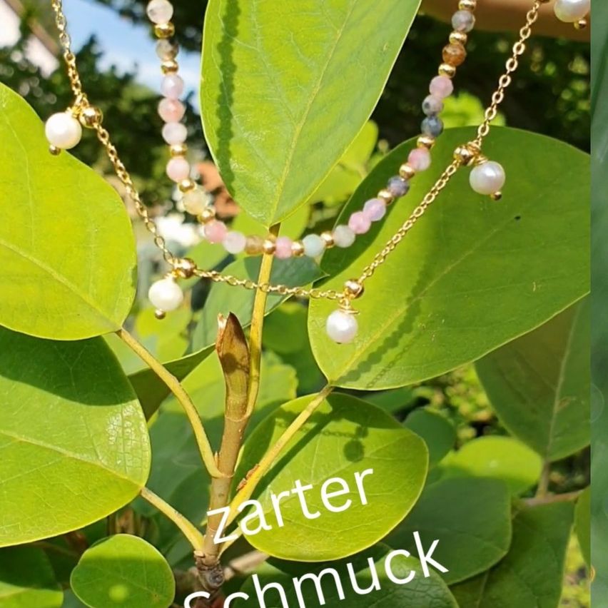 Eine Nahaufnahme einer Pflanze mit zwei goldenen Halsketten, die mit rosa und weißen Perlen an ihren Blättern hängen. Das Wort 'zarter Schmuck' ist auf den Blättern geschrieben.