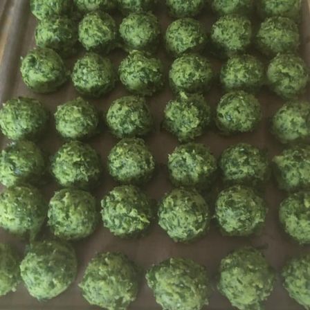 Ein Tablett gefüllt mit kleinen, runden, grünen Lebensmitteln, die wie Kugeln aussehen, möglicherweise aus Spinat oder anderen Blattgemüsen hergestellt, ordentlich in Reihen auf einem Backblech angeordnet.