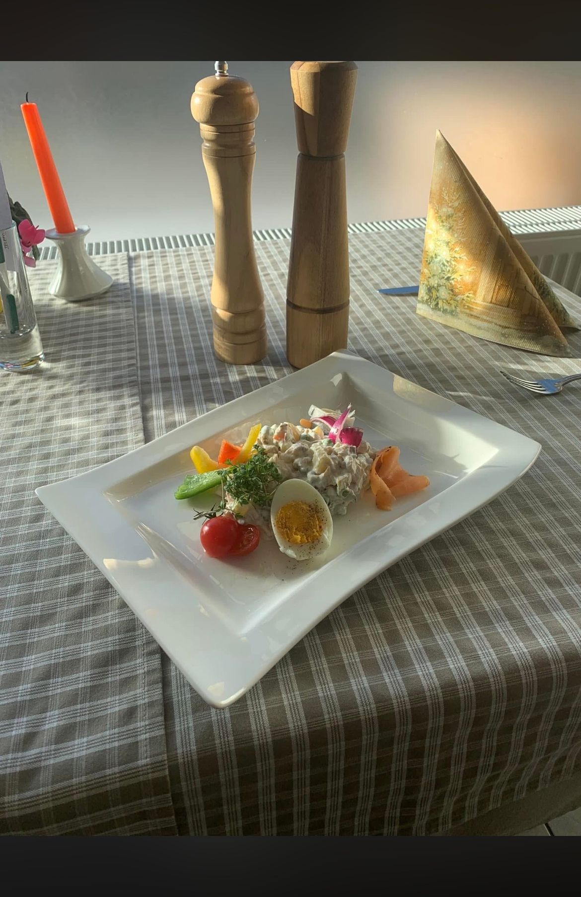 Ein weißer Teller mit Salat, einem halbgekochten Ei und Gemüse auf einem karierten Tischtuch.