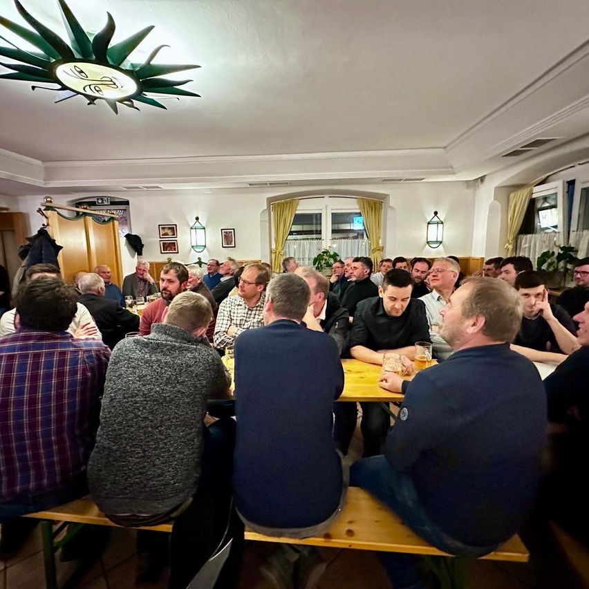 Eine Gruppe von Männern sitzt um einen Tisch in einem Restaurant, einige schauen auf etwas auf dem Tisch. Gläser und Teller sind auf dem Tisch.