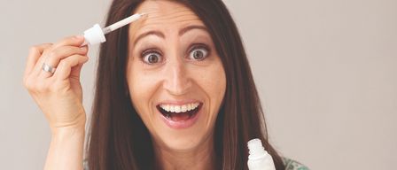 Eine Frau in einem Blumenkleid trägt mit einem Tropfenzähler einen Tropfen Serum auf ihre Stirn auf.