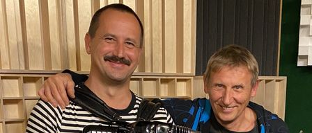 Zwei Männer in einem Studio, einer mit einem Akkordeon und der andere mit einer Saxophon, lächelnd und posieren für ein Foto.