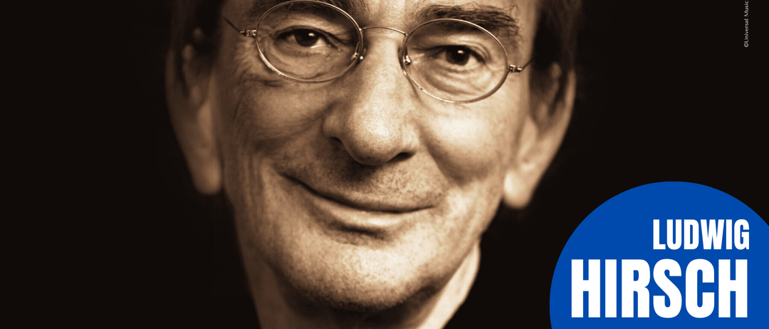 Ein monochromatisches Porträt eines Mannes mit runden Brillengläsern. Er lächelt und zeigt seine Zähne. In der unteren rechten Ecke befindet sich ein blauer Kreis mit weißem Text.