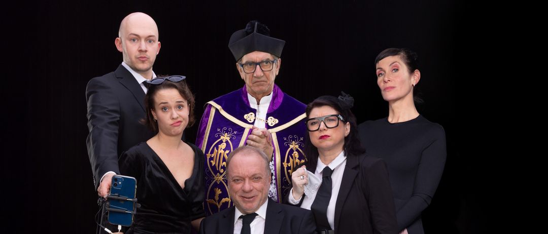 Eine Gruppe von Menschen in formeller Kleidung steht um einen sitzenden Mann mit einem Blumenstrauß herum. Sie scheinen für ein Foto zu posieren. Der Spruch auf dem Banner lautet 'in Frieden'.