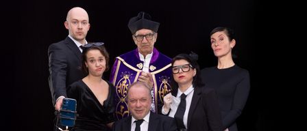 Eine Gruppe von Menschen in formeller Kleidung steht um einen sitzenden Mann mit einem Blumenstrauß herum. Sie scheinen für ein Foto zu posieren. Der Spruch auf dem Banner lautet 'in Frieden'.