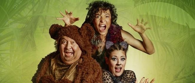 Drei Personen in Kostümen posieren vor einem grünen Hintergrund. Der Mann vorne trägt ein Bärenkostüm, während die anderen als Katze und eine weitere Person gekleidet sind.