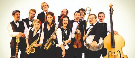 A group of musicians, dressed in formal attire, are posing for a photograph. They hold various instruments such as a saxophone, violin, drum, and guitar. They appear to be a jazz band.