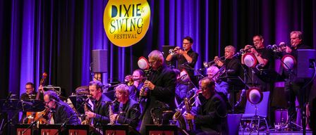 Eine Band spielt auf der Bühne unter dem Logo des Dixie & Swing Festivals, mit Musikern, die Trompeten, Saxophone und andere Instrumente spielen.