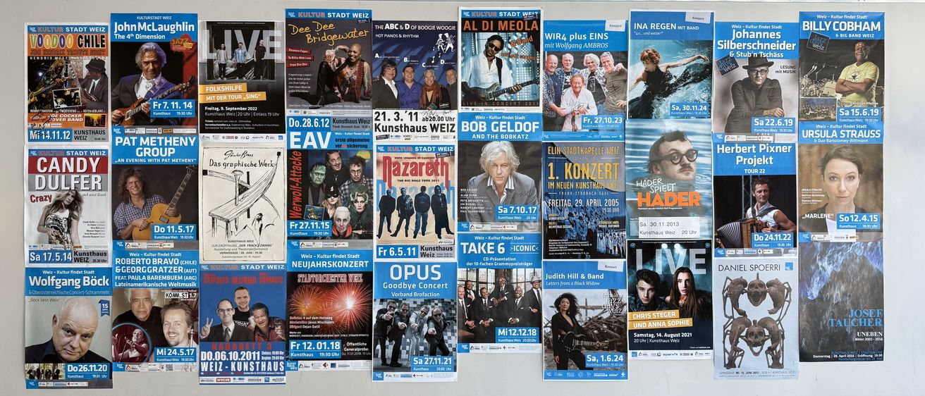 Eine Wand mit mehreren Postern. Verschiedene Veranstaltungen und Bands werden beworben, darunter Dee Dee Bridgewater, Al Di Meola und Bob Geldof. Daten und Uhrzeiten sind aufgeführt.