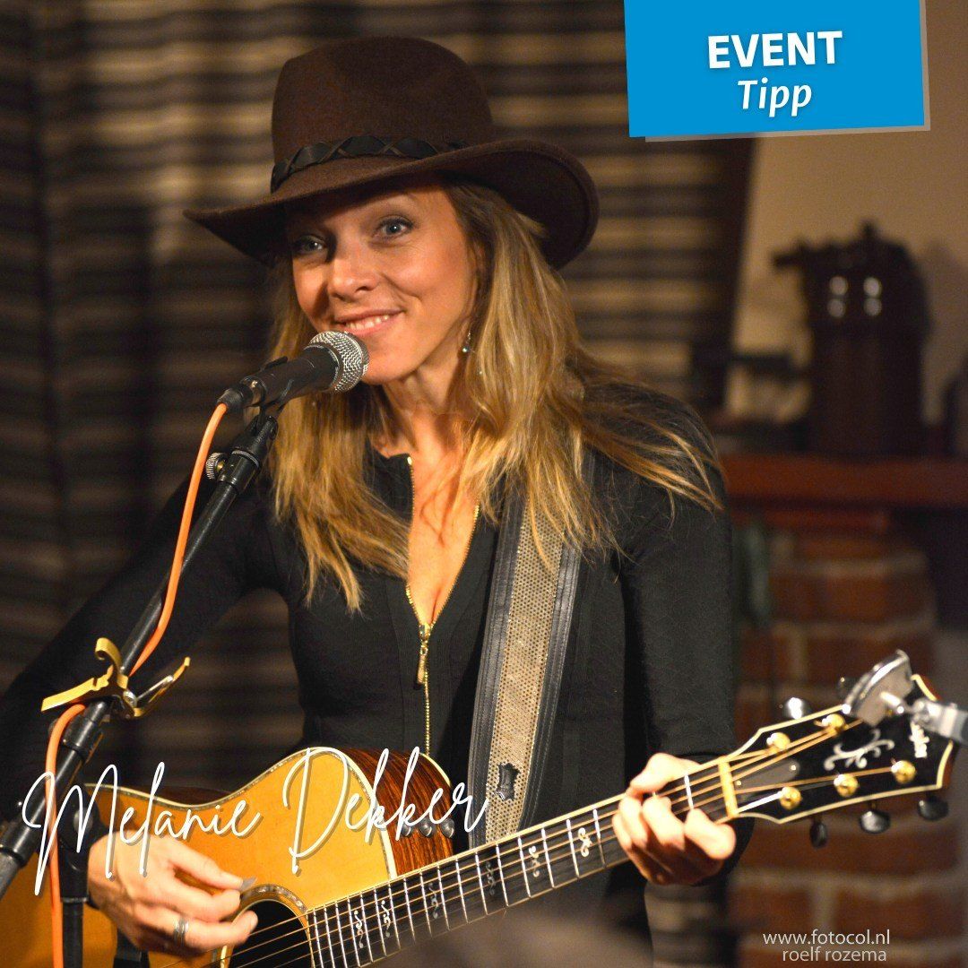 Eine Frau in einem schwarzen Top und Hut spielt Gitarre und singt in ein Mikrofon. Ein blauer Banner in der oberen rechten Ecke sagt 'EVENT Tipp'.