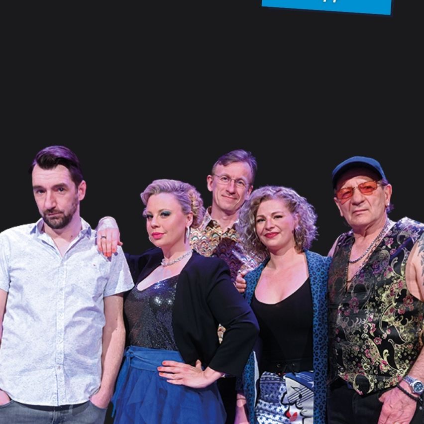 Fünf Personen stehen eng beieinander vor einem dunklen Hintergrund. Der Mann auf der linken Seite trägt ein weißes Hemd und hat die Hände in den Taschen. Neben ihm steht eine Frau mit der Hand auf seiner Schulter. Eine weitere Frau mit lockigem Haar steht in der Mitte. Der Mann auf der rechten Seite trägt eine Mütze und eine Brille.