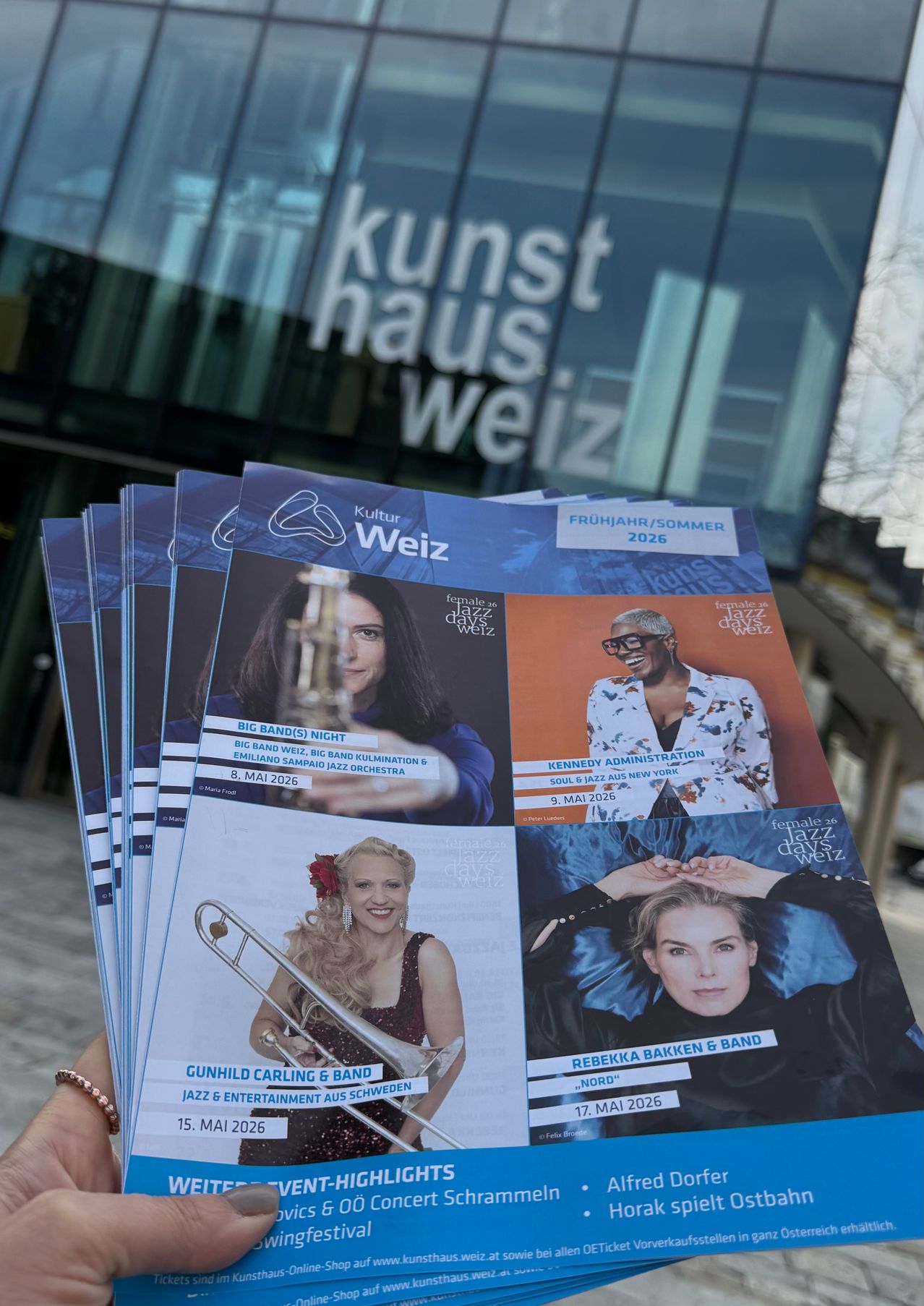 Ein Stapel Broschüren wird angezeigt, der Bilder von Musikern und Texten über verschiedene Veranstaltungen bei Kultur Weiz zeigt. Die Broschüre für den 8. Mai 2026 hebt ein Big-Band-Konzert mit dem Emiliano Sampaio Jazz Orchestra hervor. Die Broschüre für den 9. Mai 2026 zeigt Kennedy Administration und Soul-Jazz. Die Broschüre für den 17. Mai 2026 präsentiert Rebekka Bakken & Band.