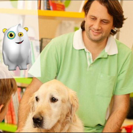 Ein Mann in einem grünen Hemd sitzt mit einem lächelnden goldenen Retriever-Hund. Hinter ihm steht ein Junge, der den Hund ansieht. Eine weiße Maskottchenfigur ist an der Wand.