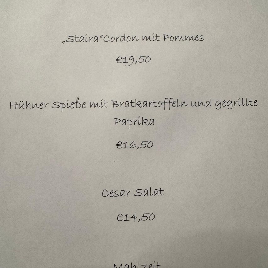 Eine Speisekarte listet drei Gerichte auf: 'Stair Cordon mit Pommes' für 19,50 Euro, 'Huhner Spiebe mit Bratkartoffeln und gegrillte Paprika' für 16,50 Euro und 'Cesar Salat' für 14,50 Euro. Jedes Gericht ist bepreist und in kursiver Schrift auf weißem Hintergrund geschrieben.