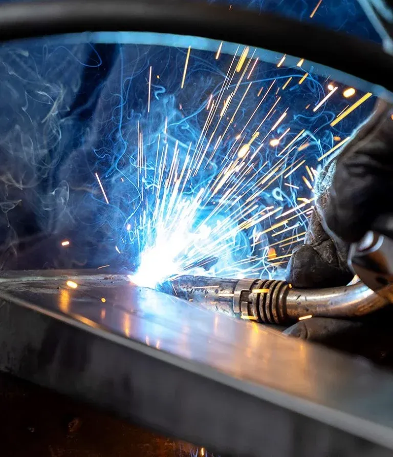 Ein Schweißer benutzt eine Fackel, um ein Metallblech zu schweißen und erzeugt dabei Funken und Rauch.