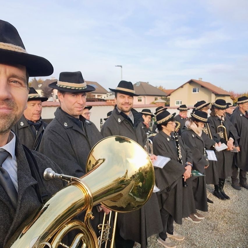 Eine Gruppe von Musikern in schwarzen Uniformen und Hüten steht in einer Reihe, wahrscheinlich für eine Aufführung, mit Häusern im Hintergrund.