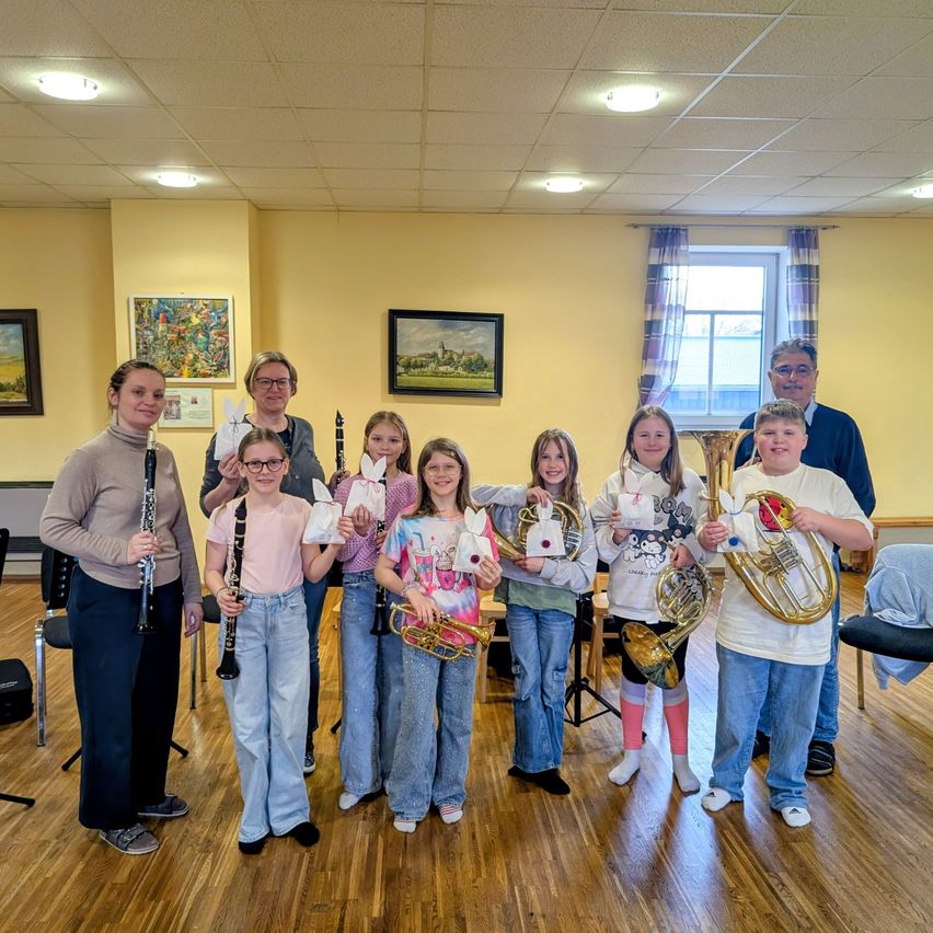 Gruppe junger Musiker, die Instrumente halten, in einem Raum mit gelben Wänden und Gemälden an der Wand.