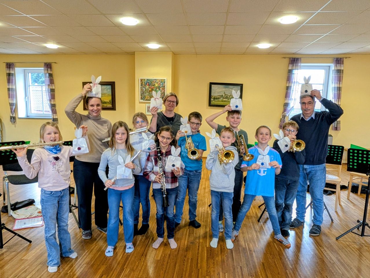 Eine Gruppe von Kindern und Erwachsenen posiert für ein Foto, während sie Instrumente halten. Sie sind alle in Freizeitkleidung gekleidet.