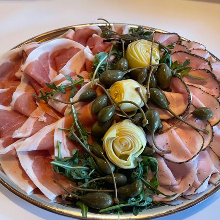 Ein Teller mit dünn geschnittenem Prosciutto, Kapern und Artischocken dekorativ arrangiert.