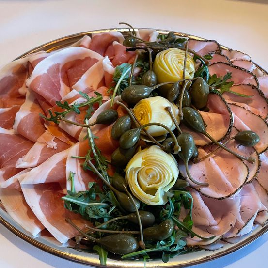 Ein Teller mit dünn geschnittenem Prosciutto, Kapern und Artischocken dekorativ arrangiert.