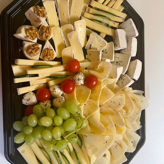 Ein schwarzer Teller mit verschiedenen Käsesorten, Trauben, Kirschtomaten und Walnüssen. Die Käsesorten sind in verschiedenen Formen und Größen und einige sind mit schwarzem Pfeffer bestreut.
