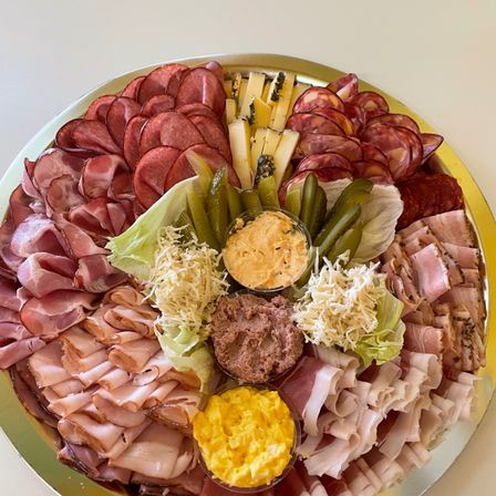Eine große Platte mit verschiedenen Fleischsorten, Käse und Beilagen in einem kreisförmigen Muster, einschließlich Salami, Schinken und Käse, begleitet von Essiggurken und verschiedenen Aufstrichen.