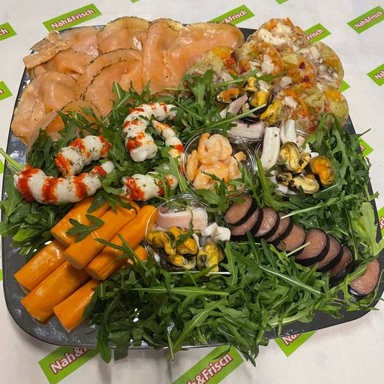Eine Platte mit verschiedenen Meeresfrüchten und Fleischsorten, einschließlich Lachs, Garnelen und Würsten, garniert mit Rucola und auf einem schwarzen Tablett serviert.