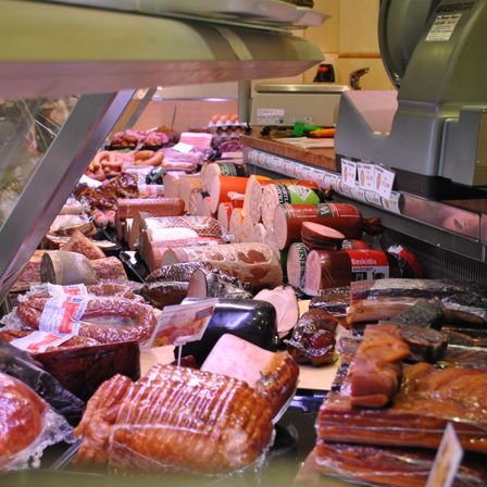 Eine Fleischtheke zeigt verschiedene Arten von Wurst und Schinken, ordentlich unter einer Glasabdeckung angeordnet. Das Sortiment umfasst Würste, Salami und andere Wurstwaren.