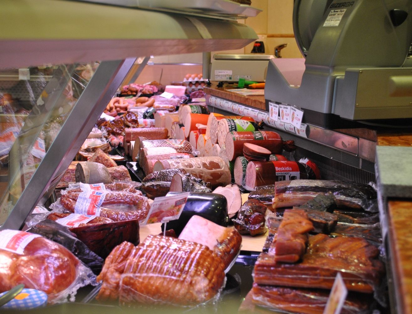 Eine Fleischtheke zeigt verschiedene Arten von Wurst und Schinken, ordentlich unter einer Glasabdeckung angeordnet. Das Sortiment umfasst Würste, Salami und andere Wurstwaren.