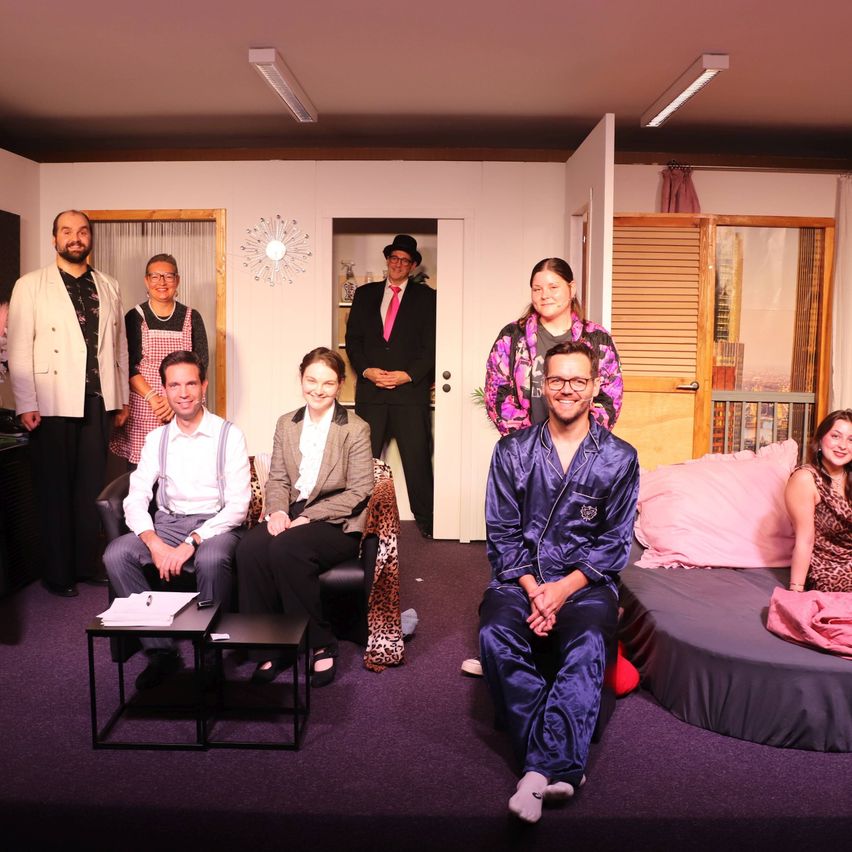 A group of people dressed in various costumes are posing for a photograph in a room with a purple carpet.