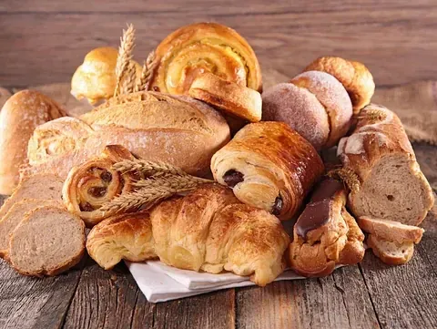 Ein Holztisch zeigt eine Auswahl an Brot und Gebäck. Verschiedene Arten umfassen Laibe, Brötchen, Croissants und Brötchen.