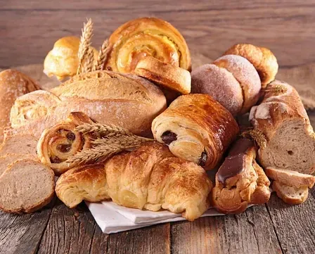 Ein Holztisch zeigt eine Auswahl an Brot und Gebäck. Verschiedene Arten umfassen Laibe, Brötchen, Croissants und Brötchen.