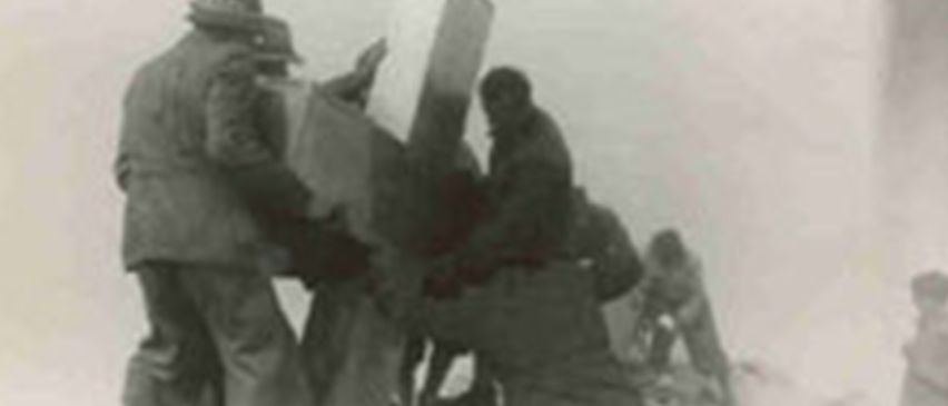 Ein Schwarz-Weiß-Bild von Soldaten, die an einer großen Waffe arbeiten. Ein Soldat sitzt auf der Waffe, und andere stehen in der Nähe und bereiten sie möglicherweise für den Einsatz vor.