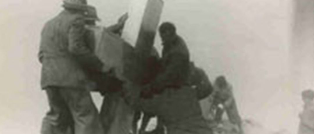 Ein Schwarz-Weiß-Bild von Soldaten, die an einer großen Waffe arbeiten. Ein Soldat sitzt auf der Waffe, und andere stehen in der Nähe und bereiten sie möglicherweise für den Einsatz vor.