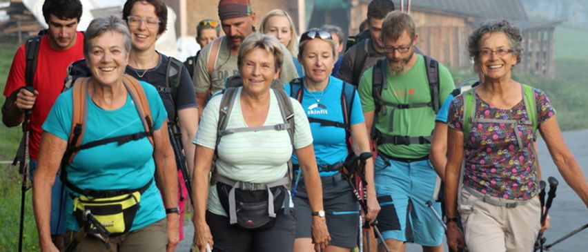 Eine Gruppe von Menschen beim Wandern, darunter eine Frau in einem weißen T-Shirt, ein Mann in einem grünen T-Shirt und andere mit Rucksäcken und Wanderausrüstung.
