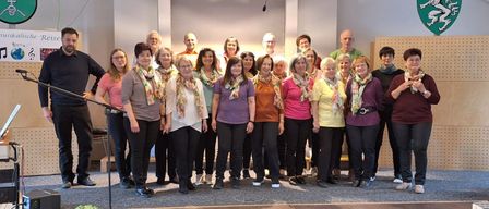 Eine Gruppe von Menschen mit Schals posiert für ein Foto auf der Bühne. Einige lächeln und schauen in die Kamera.