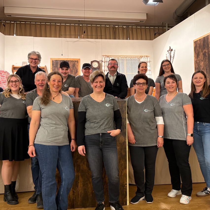 Eine Gruppe von Menschen in grauen T-Shirts und Jeans posiert für ein Foto in einem Raum mit Holzwänden und einem Holztisch.