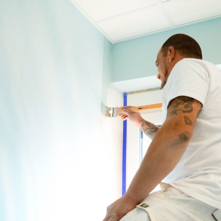 Ein Mann mit Tätowierungen an den Armen malt eine blaue Wand mit einem Pinsel.