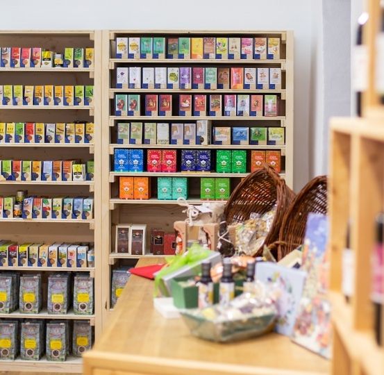 Ein Geschäft mit ordentlich gestapelten Schachteln in verschiedenen Farben, auf Holzregalen an einer weißen Wand platziert, mit einem Holztisch und Körben in der Nähe.