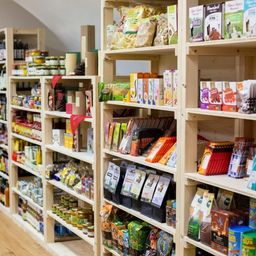 Ein Lebensmittelgeschäft mit Holzregalen, die mit verschiedenen Produkten bestückt sind. Zu den Produkten gehören Snacks, Cerealien und Konserven. Die Regale sind ordentlich organisiert und übersichtlich angeordnet. Der Laden hat einen Holzboden.