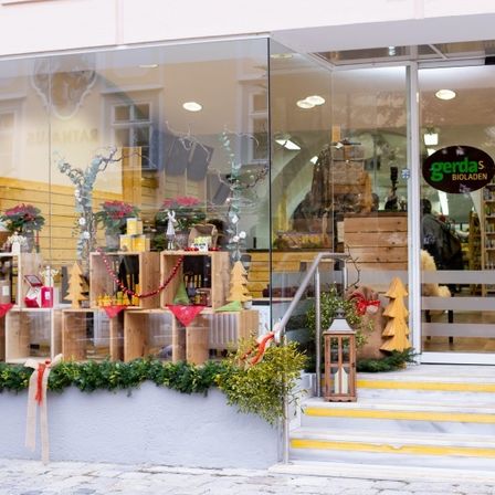 Ein Geschäft mit Glaswänden zeigt verschiedene Holzkisten und Gegenstände, möglicherweise zum Verkauf. Die Regale im Inneren sind mit Produkten bestückt und der Eingang hat ein Holzgitter.