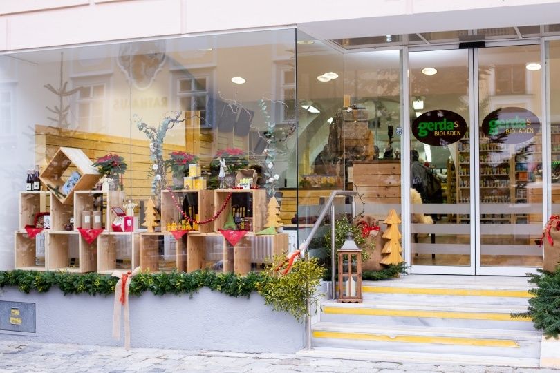 Ein Geschäft mit Glaswänden zeigt verschiedene Holzkisten und Gegenstände, möglicherweise zum Verkauf. Die Regale im Inneren sind mit Produkten bestückt und der Eingang hat ein Holzgitter.