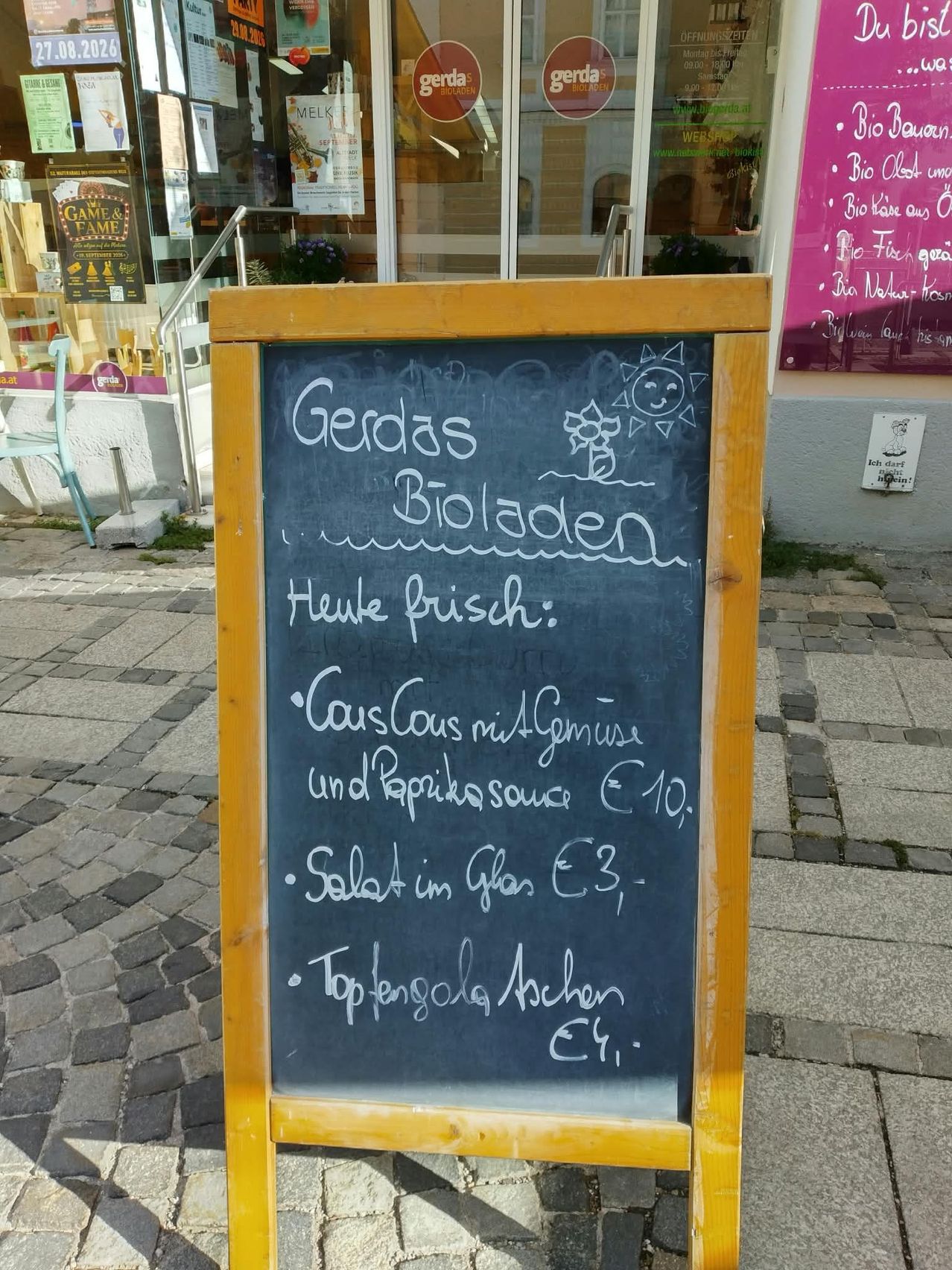 Ein Kreidetafel-Menü vor einem Geschäft mit handgeschriebenem deutschen Text, der Speisen und Preise auflistet.