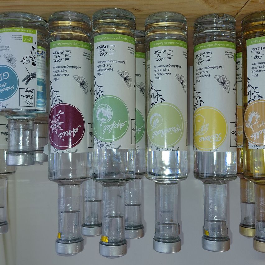Eine Reihe von Glasflaschen mit verschieden farbigen Etiketten. Die Etiketten sind rund und haben weißen Text mit grünen und gelben Designs. Die Flaschen sind in einer Reihe aufgestellt.