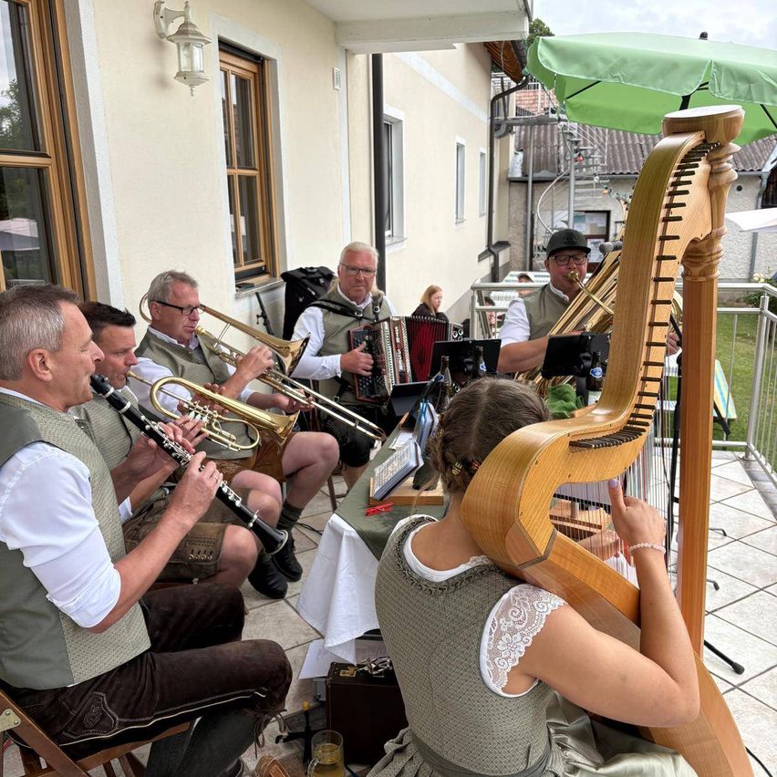 Eine Gruppe von Musikern, darunter eine Frau, die eine Harfe spielt, tritt auf einem Balkon auf. Sie sind in traditioneller Kleidung gekleidet.