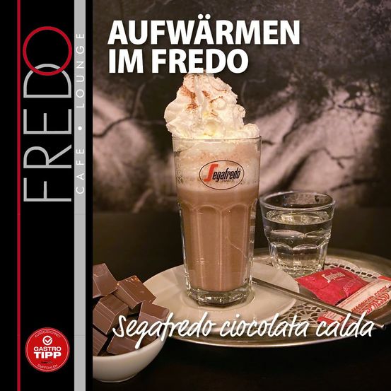 Ein Glas Segafredo Schokoladengetränk mit Schlagsahne, begleitet von einem Glas Wasser, einer Schüssel mit Schokoladenstücken und einer Zuckerpackung. Das Bild ist vor einem dunklen Hintergrund mit dem Text 'Aufwärmen im Fredo'.