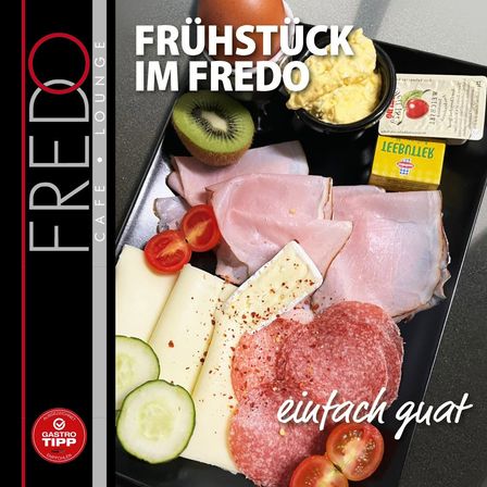 Ein Frühstücksteller im Fredo mit Schinken, Käse, Tomaten, Gurken und Kiwi. Der Teller steht auf einer schwarzen Oberfläche mit einer Schüssel mit Rührei und einer Packung Butter. Der Text lautet 'Frühstück im Fredo'.
